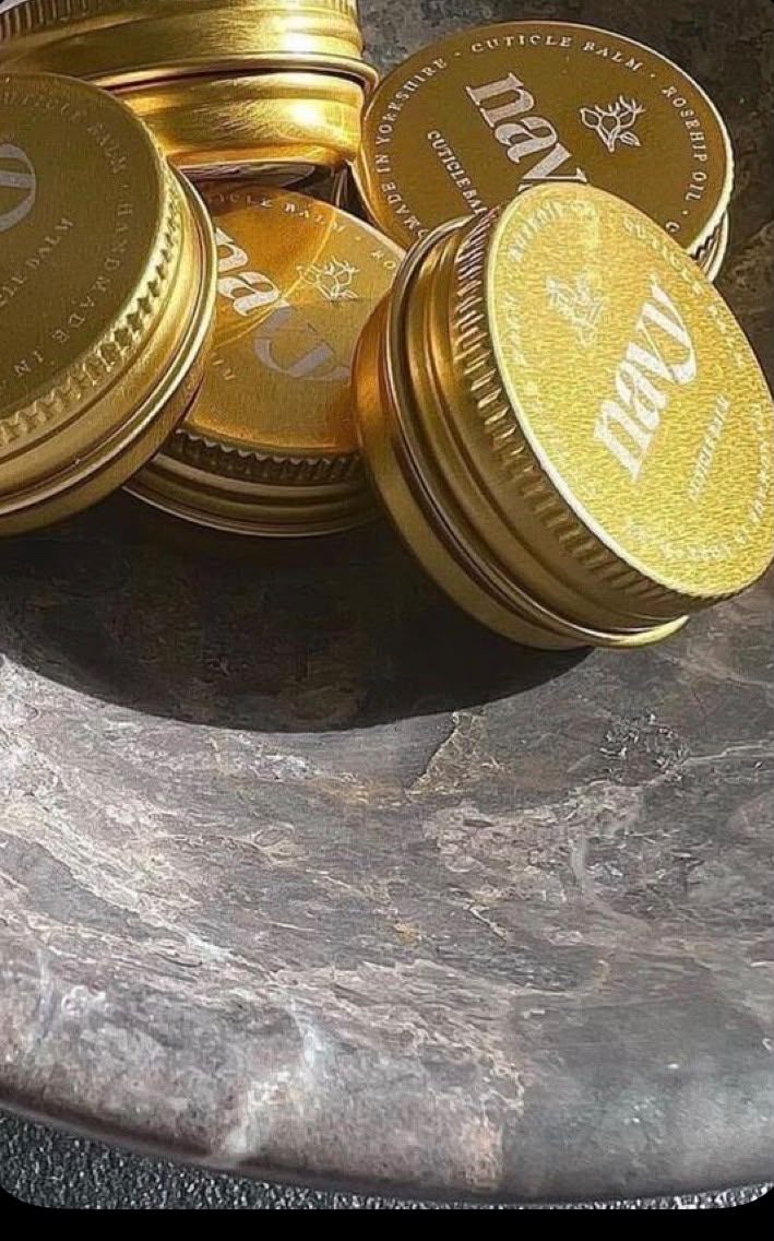 Gold tins of cuticle balm resting on a dark marble dish in the sunlight