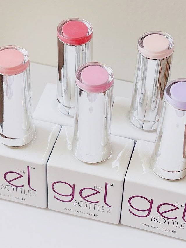 A row of gel polish bottles with silver caps in soft pink, coral and lilac shades